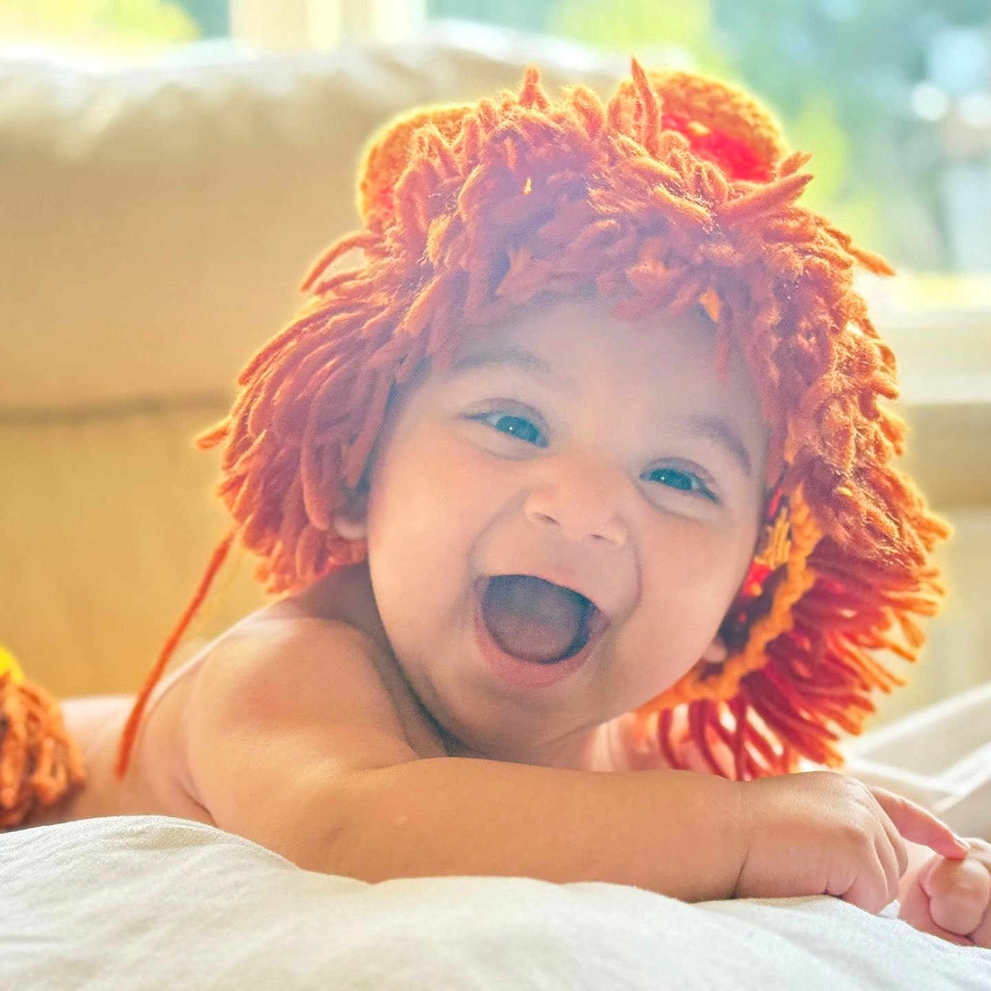 Dawar is registered to the contest to win money with this photo: baby, child, cozy, cute, expression, face, happy, indoors, infant, lying_down, orange_wig, playful, portrait, skin, smiling, soft_light, toddler, white_bedding, window, yarn_hat