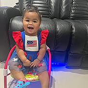 Nazly Aguilar joined the competition — help win amazing prizes! child, toddler, smiling, sitting, chair, dress, red, blue, white, flag, hair, pigtails, shoes, indoor, floor, leather_couch, happy, cute, person, portrait