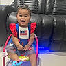 child, toddler, smiling, sitting, chair, dress, red, blue, white, flag, hair, pigtails, shoes, indoor, floor, leather_couch, happy, cute, person, portrait