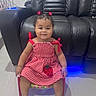 Nazly C. Aguilar joined the competition — help win amazing prizes! accessory, baby, chair, checkered_pattern, child, cute, floor, footwear, hair_clips, happy, indoors, leather_couch, person, red_dress, seated, smiling, strawberry_patch, toddler, white_shoes, young_child