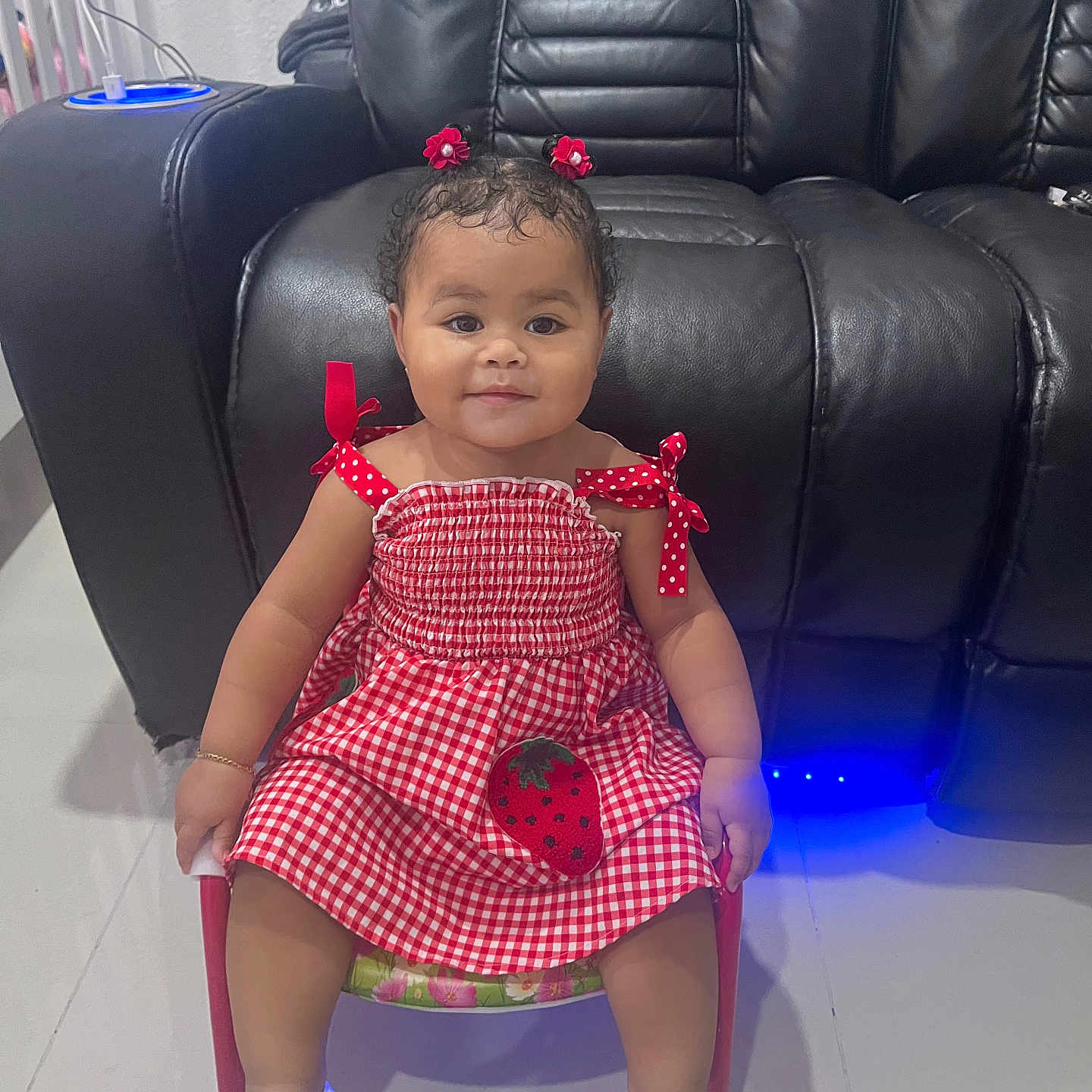 Nazly C. Aguilar joined the competition — help win amazing prizes! accessory, baby, chair, checkered_pattern, child, cute, floor, footwear, hair_clips, happy, indoors, leather_couch, person, red_dress, seated, smiling, strawberry_patch, toddler, white_shoes, young_child