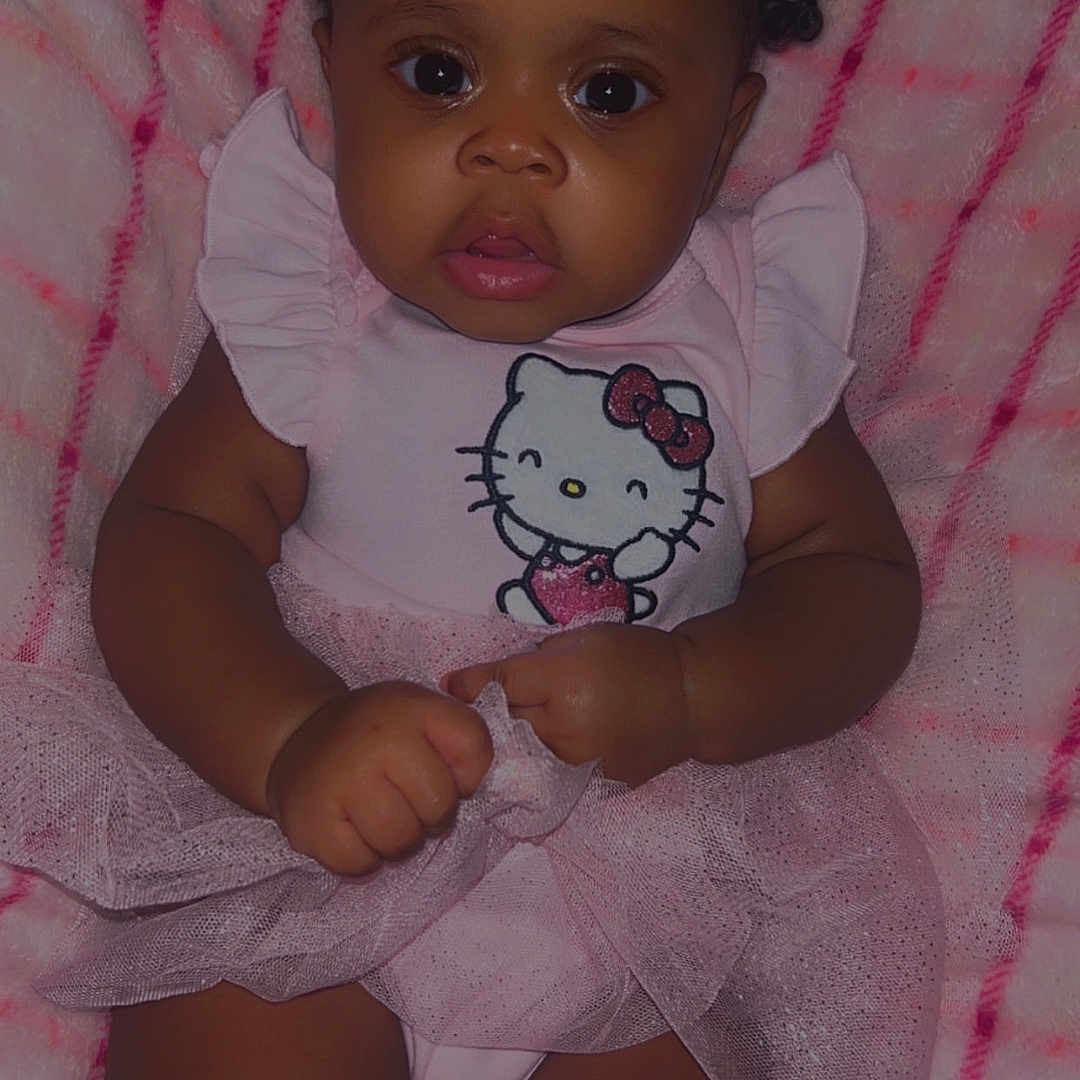 Onaraya is registered to the contest to win money with this photo: baby, blanket, bow, child, chubby_arms, chubby_legs, clothing, curly_hair, cute, dress, hand, hello_kitty, indoors, infant, person, pink, portrait, smiling, soft_texture, tutu