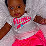 Onaraya is registered to the contest to win money with this photo: baby, bow, child, closeup, clothing, cute, dark_skin, face, fluffy_blanket, happy, indoors, infant, lying_down, person, pink_shorts, portrait, puma, smiling, tshirt, young_child