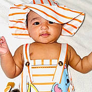 Zane is registered to the contest to win money with this photo: baby, child, infant, hat, striped_clothing, animal_print, giraffe_toy, plush_toy, soft_blanket, smiling, portrait, cute, lying_down, colorful, striped_hat, buttoned_straps, indoors, young_child, face, eyes