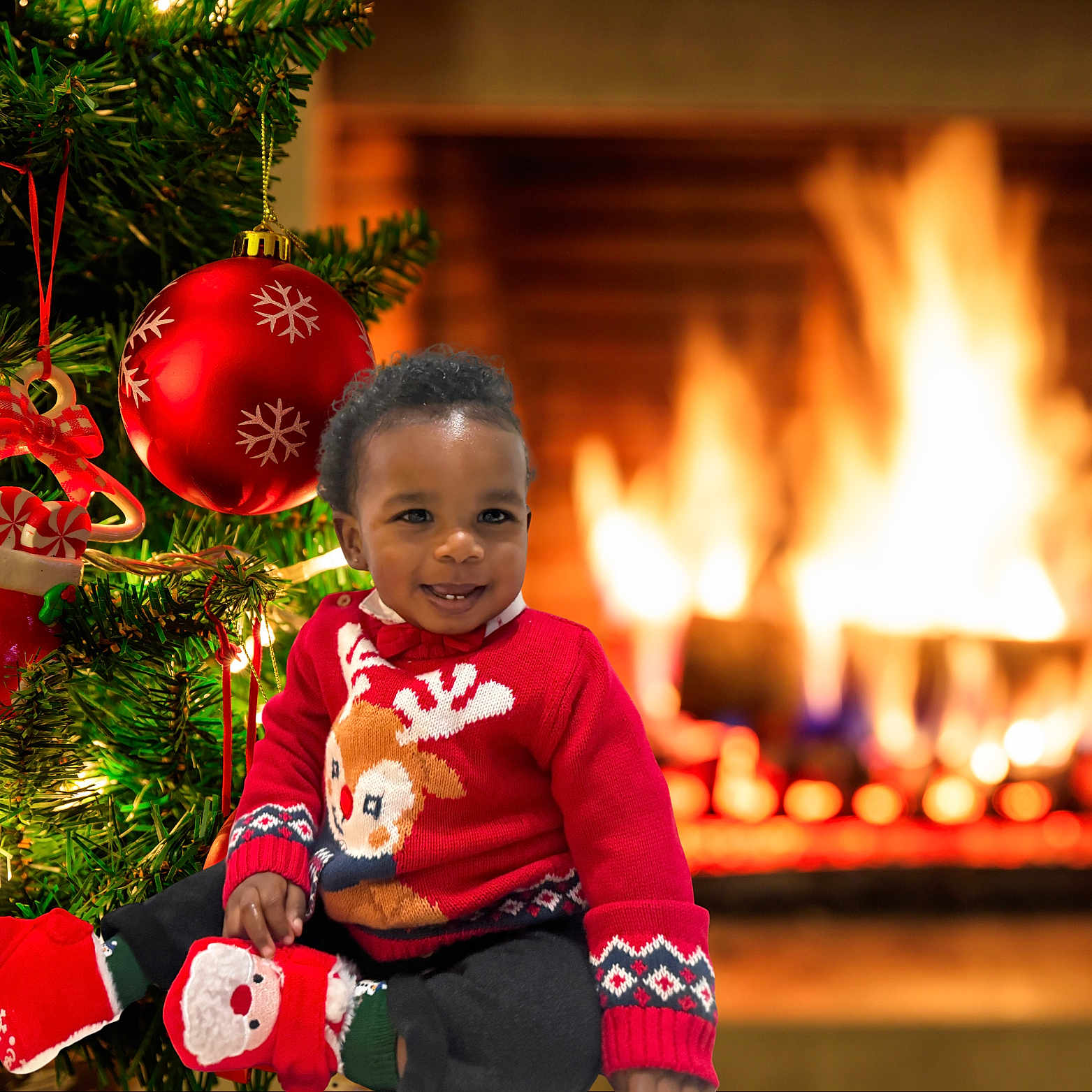 Baby Bear is registered to the contest to win money with this photo: toddler, child, christmas_tree, christmas_ornament, fireplace, holiday, festive_clothing, reindeer_sweater, santa_slippers, smiling, indoors, warmth, decorations, celebration, holiday_lights, cozy, happy, seasonal, festive, cute