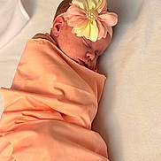 Enid is registered to the contest to win money with this photo: newborn, baby, sleeping, blanket, headband, flower, peach, pastel, soft, cozy, closeup, infant, wrapped, resting, peaceful, cute, child, portrait, indoors, comfort