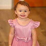 Taylor is registered to the contest to win money with this photo: child, girl, toddler, pink_dress, formalwear, hair_bow, smiling, portrait, standing, indoors, wooden_door, hardwood_floor, home, fashion, celebration, cute, young_child, dress, facial_expression, full_body