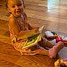 Taylor joined the competition — help win amazing prizes! child, toddler, girl, smiling, sitting, reading, book, toy, playroom, indoors, wooden_floor, floral_dress, pink_socks, colorful, portrait, happy, face, home, basket, rug