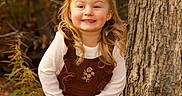 Cadence is registered to the contest to win money with this photo: child, girl, smiling, portrait, outdoors, autumn, forest, woodland, tree, tree_trunk, fallen_leaves, brown_dress, white_shirt, blonde_hair, sitting, rock, nature, golden_light, happy, fashion