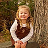 child, girl, smiling, portrait, outdoors, autumn, forest, woodland, tree, tree_trunk, fallen_leaves, brown_dress, white_shirt, blonde_hair, sitting, rock, nature, golden_light, happy, fashion