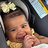 baby, child, car_seat, yellow_bow, yellow_clothing, smiling, hands, bracelet, blanket, cute, infant, portrait, indoors, seatbelt_warning, face, closeup, happy, hair, skin, person