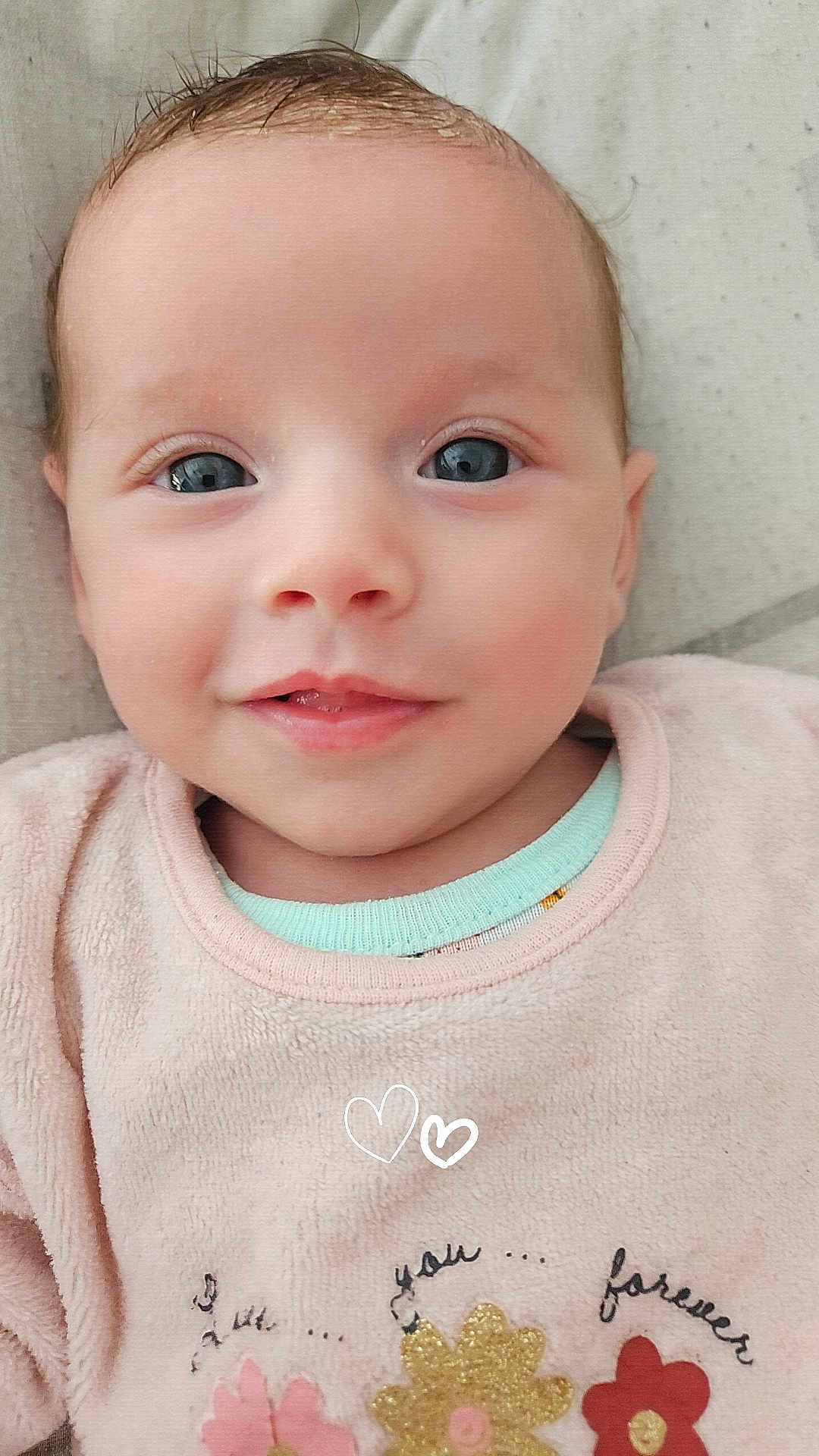 Mackenzie a rejoint le concours — aidez-le/la à gagner de superbes lots ! baby, blue_eyes, cheeks, closeup, cute, eyelashes, face, floral_pattern, head, infant, lying_down, mouth, nose, pink_clothing, portrait, skin, smile, soft_texture, toddler, young_child