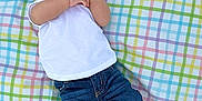 Ares is registered to the contest to win money with this photo: baby, infant, child, plaid_blanket, white_shirt, blue_jeans, brown_shoes, lying_down, cute, hands, face, relaxed, outdoor, pattern, colorful, clothing, portrait, small_child, footwear, casual