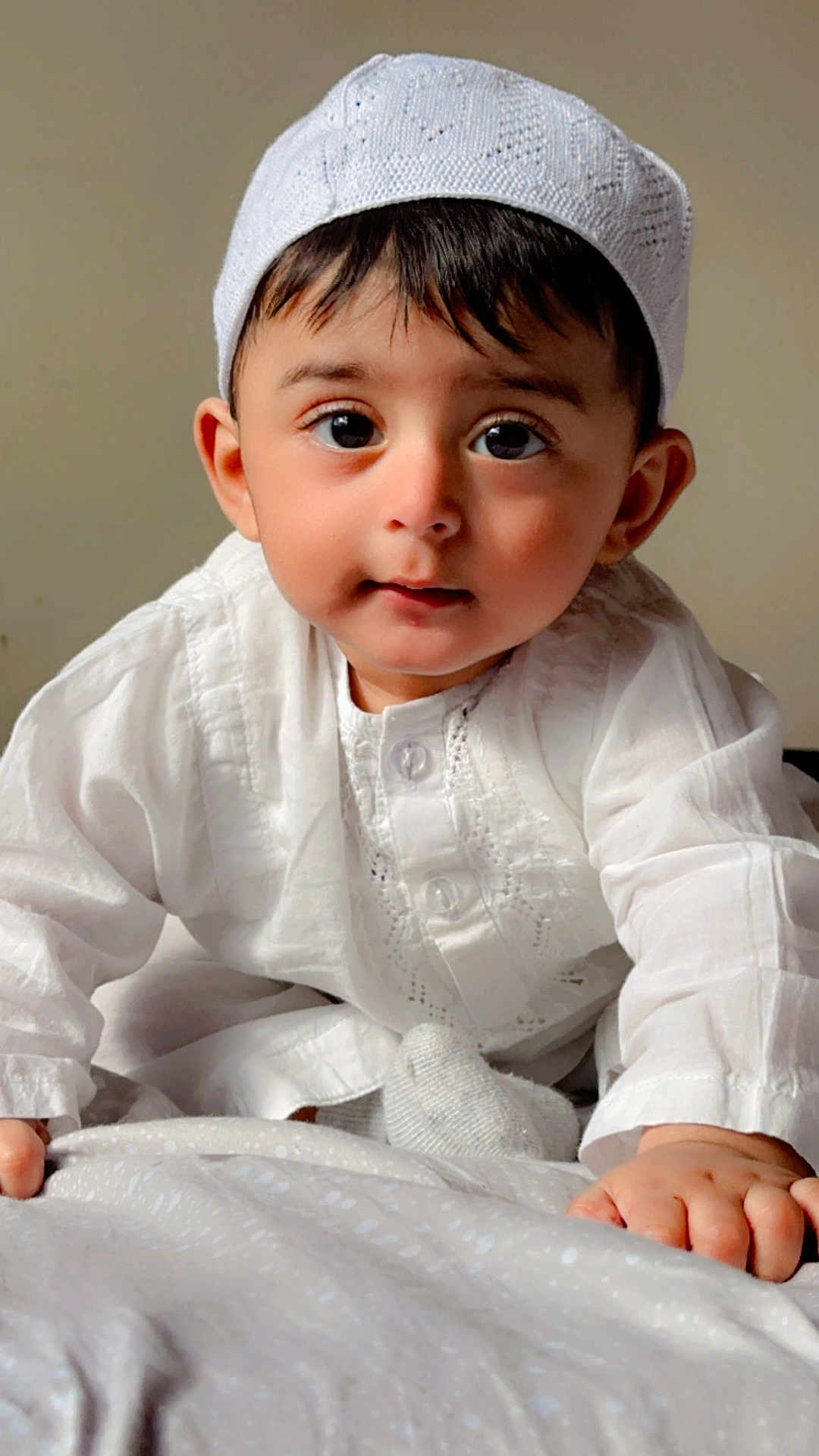 Muhammad joined the competition — help win amazing prizes! baby, child, infant, cute, white_clothing, cap, crawling, hands, face, big_eyes, soft_texture, patterned_surface, neutral_background, portrait, indoors, closeup, young_child, expression, person, adorable