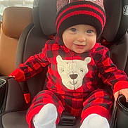 Noah is registered to the contest to win money with this photo: baby, child, car_seat, hat, pom_pom, onesie, red_and_black, plaid, smiling, socks, car_interior, seatbelt, face, winter_clothing, cute, infant, vehicle, window, daylight, portrait