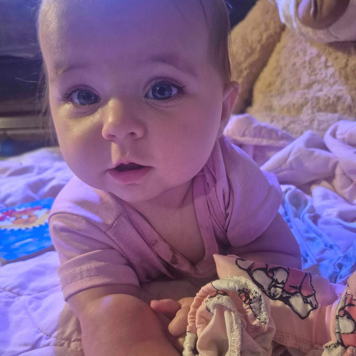 Lynda is registered to the contest to win money with this photo: baby, bedroom, blanket, child, childhood, close_up, cozy, curious, cute, eyes, face, hands, indoor, infant, lying_down, pink_shirt, portrait, sleepwear, soft_toys, teddy_bear