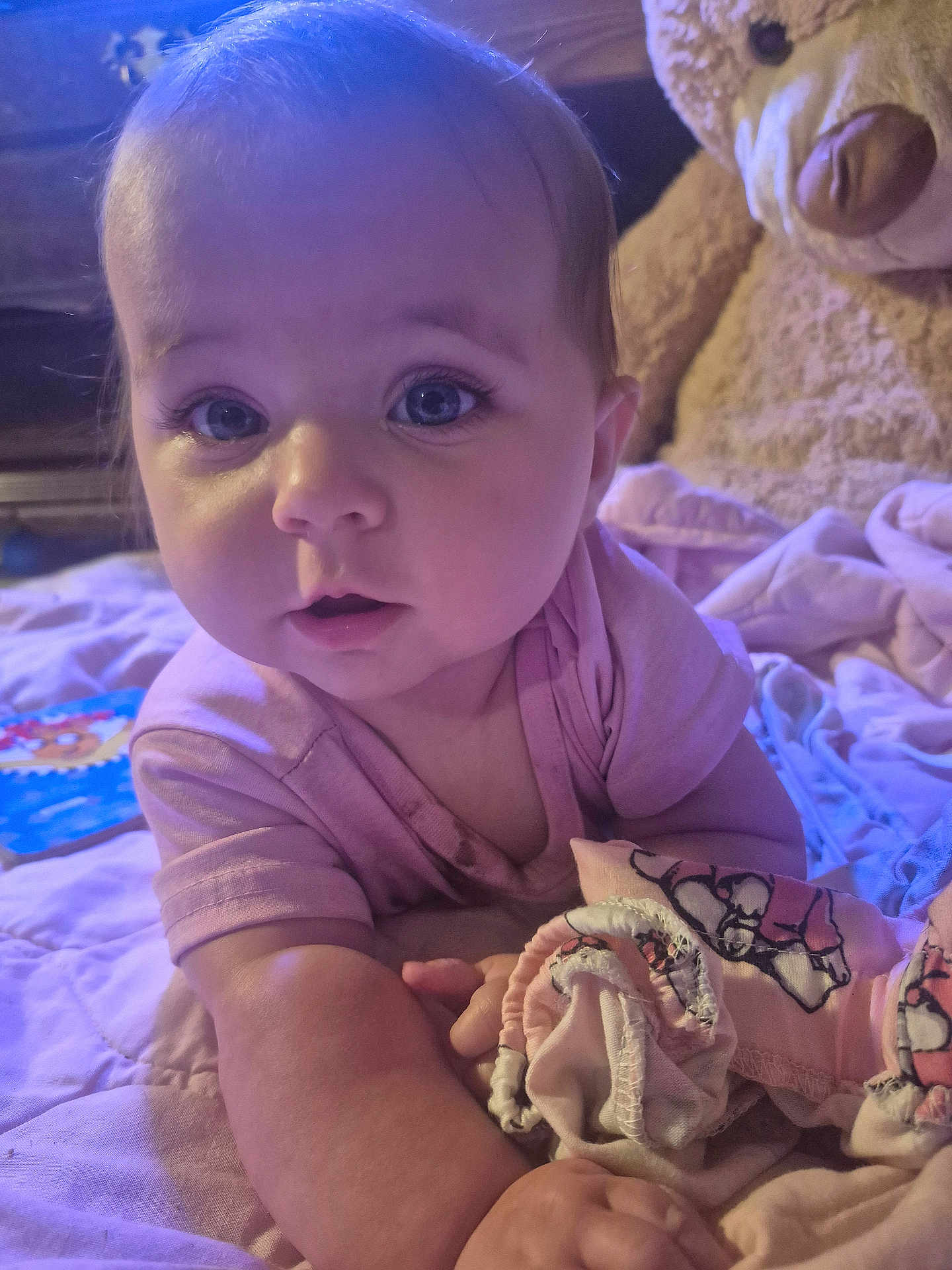 Lynda is registered to the contest to win money with this photo: baby, bedroom, blanket, child, childhood, close_up, cozy, curious, cute, eyes, face, hands, indoor, infant, lying_down, pink_shirt, portrait, sleepwear, soft_toys, teddy_bear