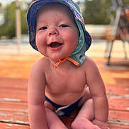 Eli is registered to the contest to win money with this photo: baby, child, hat, smiling, happy, sitting, outdoor, wooden_deck, sun_hat, bare_chest, infant, cute, summer, nature, portrait, daylight, skin, feet, hands, playful