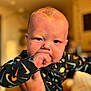 Eli joined the competition — help win amazing prizes! baby, child, infant, face, hand, fist, clothing, patterned_clothing, indoor, blurred_background, warm_lighting, person, cute, expression, skin, head, hair, portrait, closeup, holding