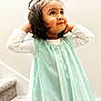 child, girl, portrait, dress, long_sleeve, standing, stairs, carpet, wall, indoor, curly_hair, playful, cute, young, smiling, looking_up, light_colored_clothing, casual, happy, innocent