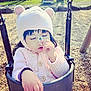 child, swing, hat, flower, pink_sweater, playground, outdoor, wood_chips, tree, daylight, cute, cold_weather, baby, holding, seat, nature, person, park, curly_hair, pensive