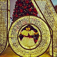 Robin is registered to the contest to win money with this photo: child, toddler, christmas_tree, christmas_decoration, lights, festive_clothing, holiday, red_ornaments, indoor, celebration, smiling, cute, dress, decor, illumination, winter, happy, framed, posing, event