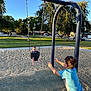 baby, child, swing, playground, sand, grass, trees, sunlight, outdoor, park, smiling, playing, fun, happy, blue_sky, summer, casual_clothing, person, daytime, recreation