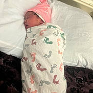 Oaklynn is registered to the contest to win money with this photo: newborn, baby, swaddled, blanket, pink_hat, sleeping, pillow, bed, footprints_pattern, infant, resting, cozy, cute, child, person, indoors, soft, warm, wrapped, peaceful