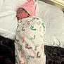 newborn, baby, swaddled, blanket, pink_hat, sleeping, pillow, bed, footprints_pattern, infant, resting, cozy, cute, child, person, indoors, soft, warm, wrapped, peaceful