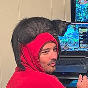 Shadow joined the competition — help win amazing prizes! man, red_hoodie, black_cat, cat_on_shoulder, computer, gaming, laptop, indoor, person, face, pet, technology, casual, leisure, screen, game, animal, companion, relaxation, hood
