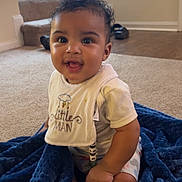 Kyrie is registered to the contest to win money with this photo: baby, child, smiling, indoor, blanket, bib, curly_hair, carpet, stairs, window, natural_light, cute, happy, sitting, infant, clothing, person, home, floor, toddler