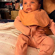 Kouture joined the competition — help win amazing prizes! baby, infant, child, portrait, sitting, peach_outfit, bib, curly_hair, wide_eyes, calm, adult, caregiver, holding, indoors, bed, bedding, home, close_up, family, photography