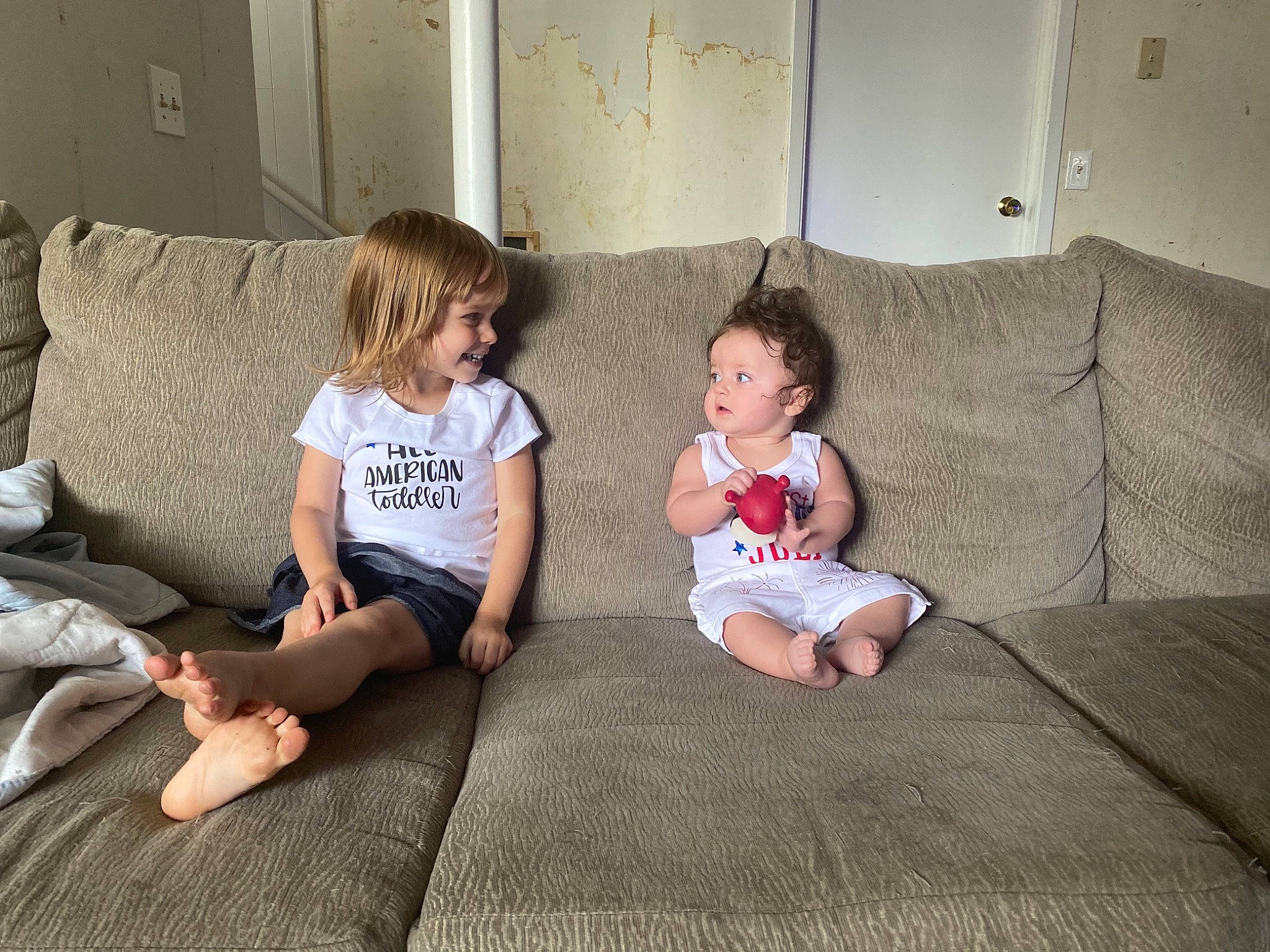 Alanah is registered to the contest to win money with this photo: baby_toddler_clothing, barefoot, child, comfort, couch, floor, flooring, foot, fun, hairstyle, hardwood, human, joy, knee, lap, living_room, person, room, shorts, sitting
