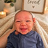 baby, newborn, smiling, blue_outfit, blanket, hand, candle, plant, framed_sign, text, cozy, indoor, portrait, cute, face, infant, warm_lighting, happy, soft_texture, love