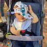 Eden a rejoint le concours — aidez-le/la à gagner de superbes lots ! baby, stroller, cap, hat, pacifier, child, outdoor, sunlight, blue_eyes, bib, clothing, seatbelt, toy, hand, smile, person, casual, colorful, playful, dinosaur_print