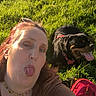 Satan participe au concours pour gagner de l'argent avec cette photo : woman, person, dog, pet, selfie, outdoor, grass, meadow, sunlight, portrait, face, tongue, smiling, funny, black_dog, tan_markings, red_collar, sunglasses, necklace, backpack