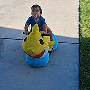 Jax joined the competition — help win amazing prizes! child, toddler, baby, dinosaur_toy, ride_on_toy, pacifier, outdoor, driveway, sidewalk, grass, sunlight, shadow, striped_shirt, seated, portrait, playtime, toy, yellow, blue, residential