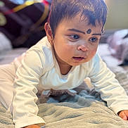 Harini is registered to the contest to win money with this photo: baby, child, crawling, blanket, indoors, soft_texture, curious, face, hand, long_sleeve, infant, portrait, young_child, eyebrows, earrings, skin, expression, bedroom, focus, cute
