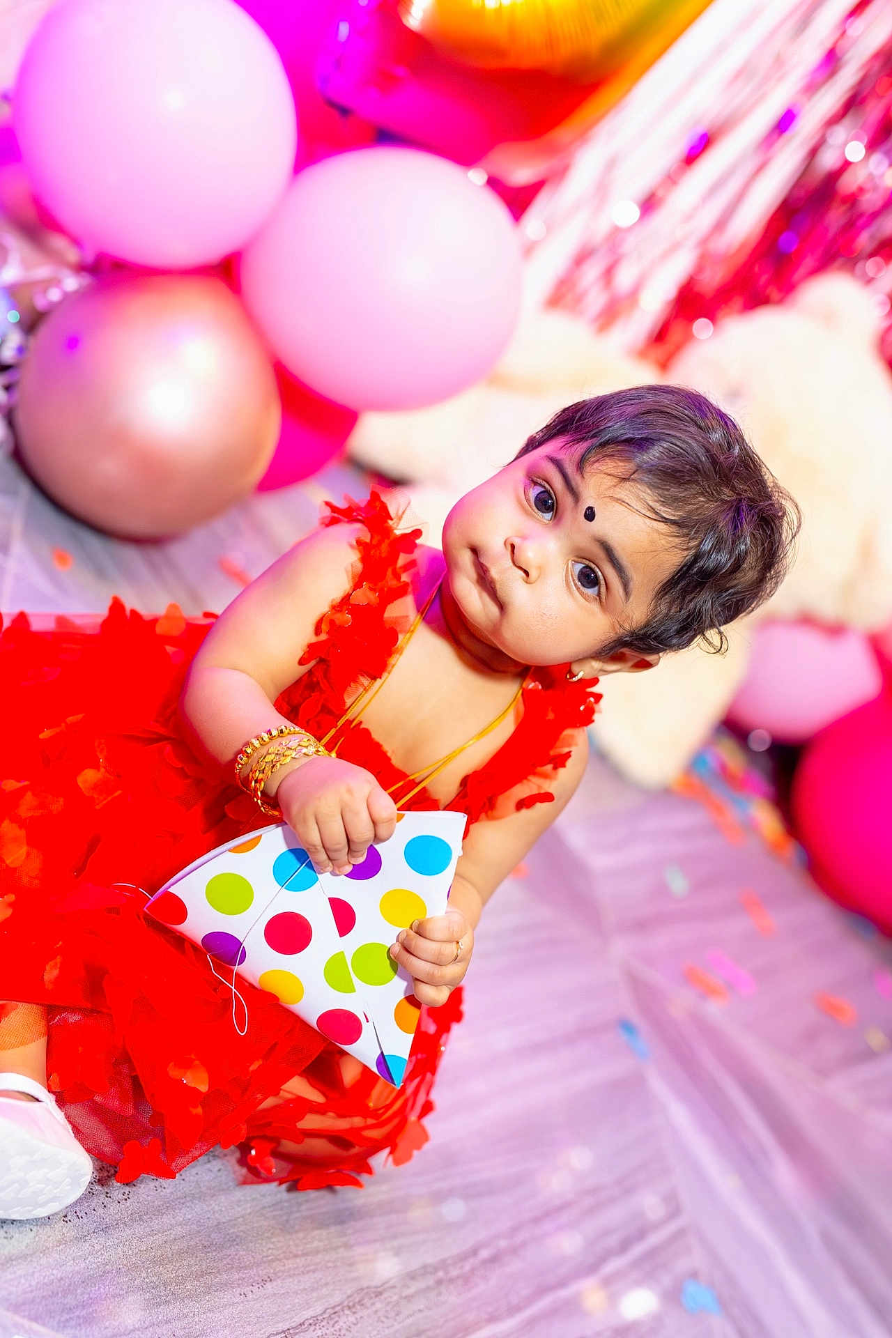 Harini is registered to the contest to win money with this photo: baby, child, red_dress, balloons, party, celebration, floor, polka_dot, hat, cute, jewelry, bracelets, indoor, decoration, confetti, portrait, smiling, festive, person, happy