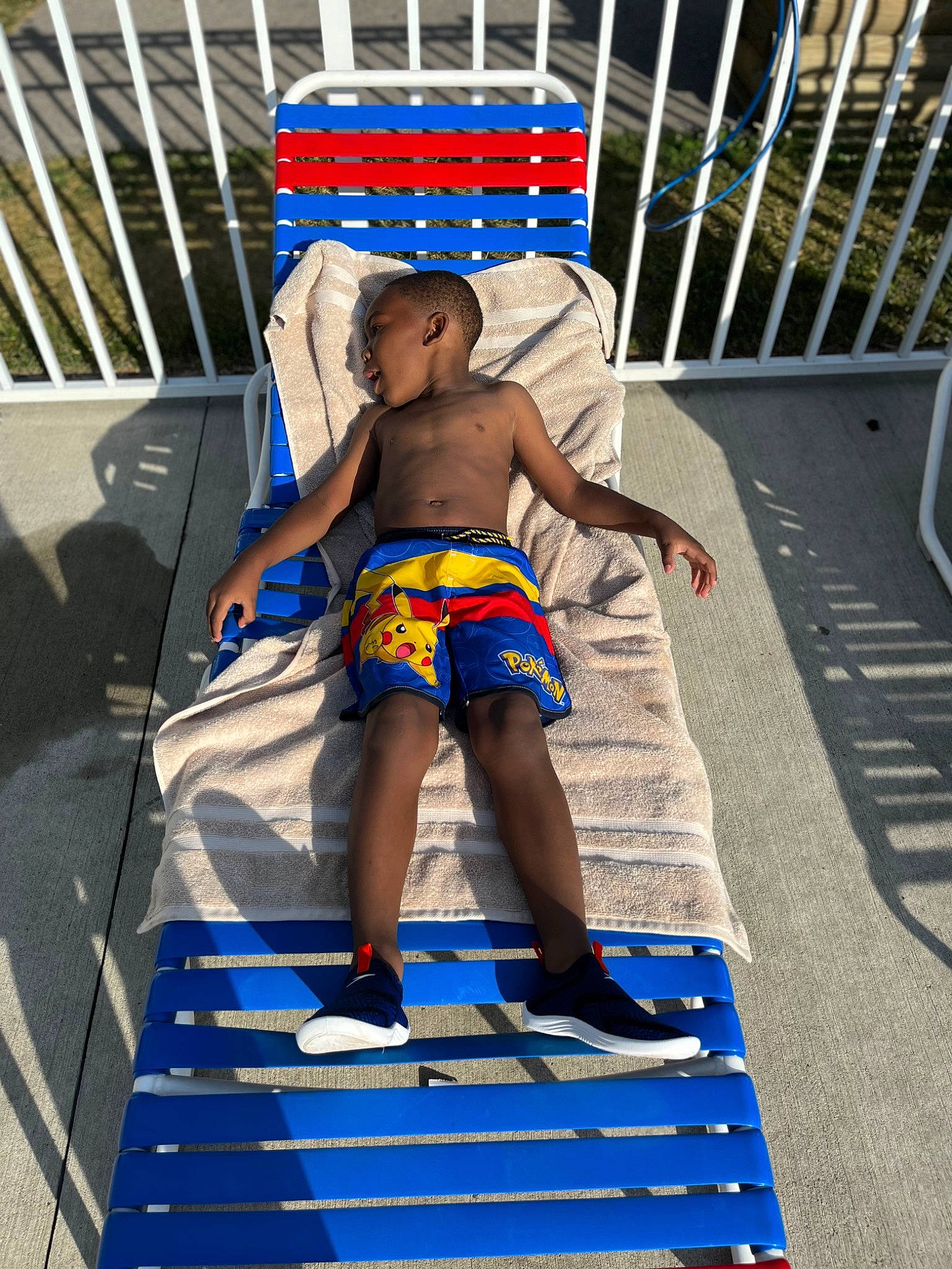 Jabari is registered to the contest to win money with this photo: barechested, barefoot, blue, board_short, calf, competition_event, electric_blue, fence, foot, fun, human_leg, leisure, outdoor_furniture, person, recreation, shorts, sitting, thigh, toddler, trunks