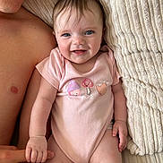 Madelyn joined the competition — help win amazing prizes! baby, infant, child, person, smiling, holding_hand, pink_onesie, mushroom_print, heart_print, blanket, textured_blanket, bare_chest, adult_hand, skin, blue_eyes, happy, lying_down, close_up, cute, indoors