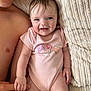 baby, infant, child, person, smiling, holding_hand, pink_onesie, mushroom_print, heart_print, blanket, textured_blanket, bare_chest, adult_hand, skin, blue_eyes, happy, lying_down, close_up, cute, indoors