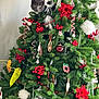 christmas_tree, cat, gray_cat, holiday_decorations, red_berries, ornaments, greenery, festive, indoor, holiday_season, pine_tree, decorated_tree, holiday_spirit, playful_cat, curious_cat, holiday_cheer, seasonal, festive_decor, christmas, holiday_fun