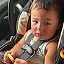 Kayden is registered to the contest to win money with this photo: child, toddler, car_seat, seatbelt, car_interior, steering_wheel, window, keychain, toy, summer_clothing, brown_hair, chubby_cheeks, portrait, close_up, sitting, safety_harness, passenger, hand, skin, roadside