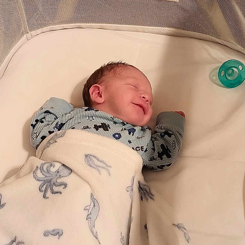 Braxton is registered to the contest to win money with this photo: newborn, baby, infant, sleeping, smiling, face, portrait, blanket, swaddle, crib, bassinet, pacifier, mitten, clothing, indoor, nursery, cozy, lying_down, bed, photography