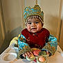 baby, child, high_chair, toy, crown, blue_clothing, gold_embroidery, smiling, indoor, cute, portrait, hands, face, person, young_child, playing, happy, seated, colorful_toy, traditional_clothing