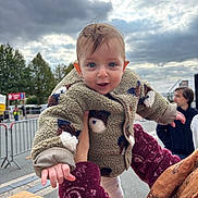 Ambre participe au concours pour gagner de l'argent avec cette photo : baby, child, person, outdoor, cloudy_sky, fleece_jacket, holding, hand, smiling, blue_eyes, curly_hair, adult, people, street, barrier, trees, casual_clothing, daytime, expression, footwear