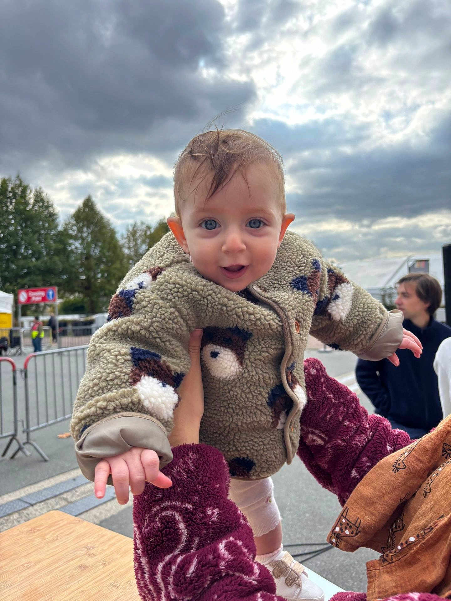 Ambre participe au concours pour gagner de l'argent avec cette photo : baby, child, person, outdoor, cloudy_sky, fleece_jacket, holding, hand, smiling, blue_eyes, curly_hair, adult, people, street, barrier, trees, casual_clothing, daytime, expression, footwear