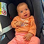 baby, child, infant, car_seat, orange_sweater, pink_pants, white_socks, smiling, happy, indoors, seatbelt, safety_label, person, cute, portrait, young_child, clothing, head, hand, face