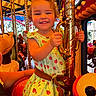child, girl, smile, carousel, amusement_park, ride, dress, ladybug_pattern, curly_hair, bow, hand, pole, colorful, fun, joy, happy, portrait, indoor, toy, person